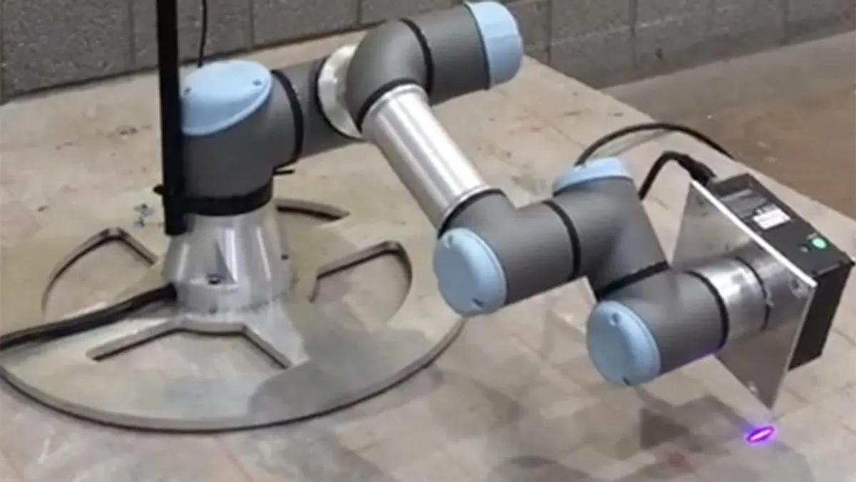 A robot sits on a bed of concrete. It&#x27;s sleek and off-white, with a visual lens on the front.