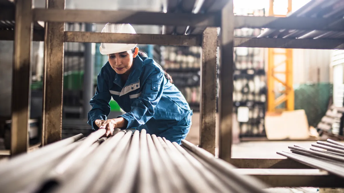 Female steel factory worker at work moving steel poles.
