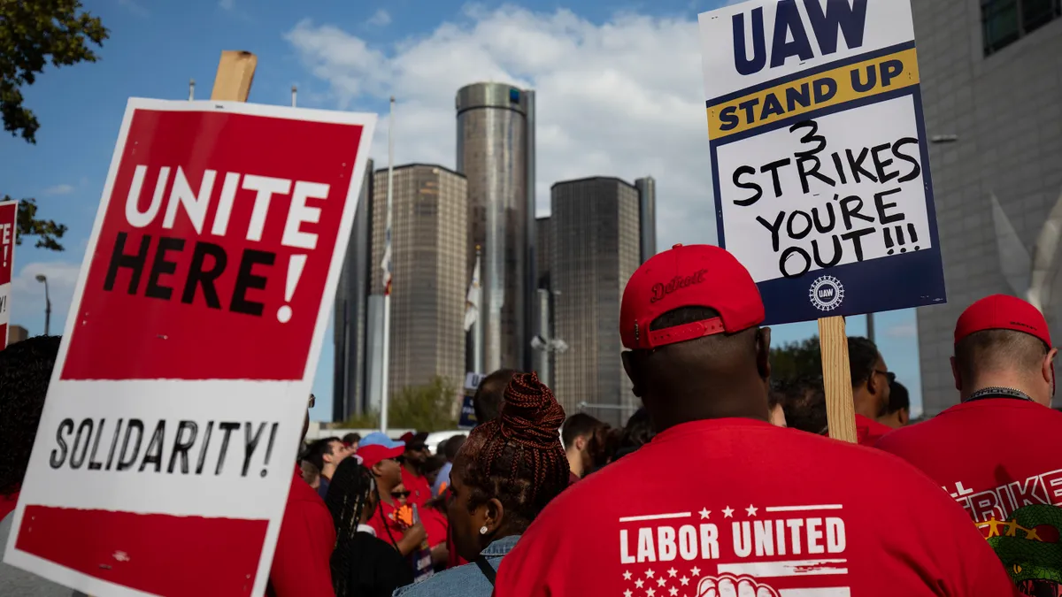 UAW union members strike holding signs with the city in the background.